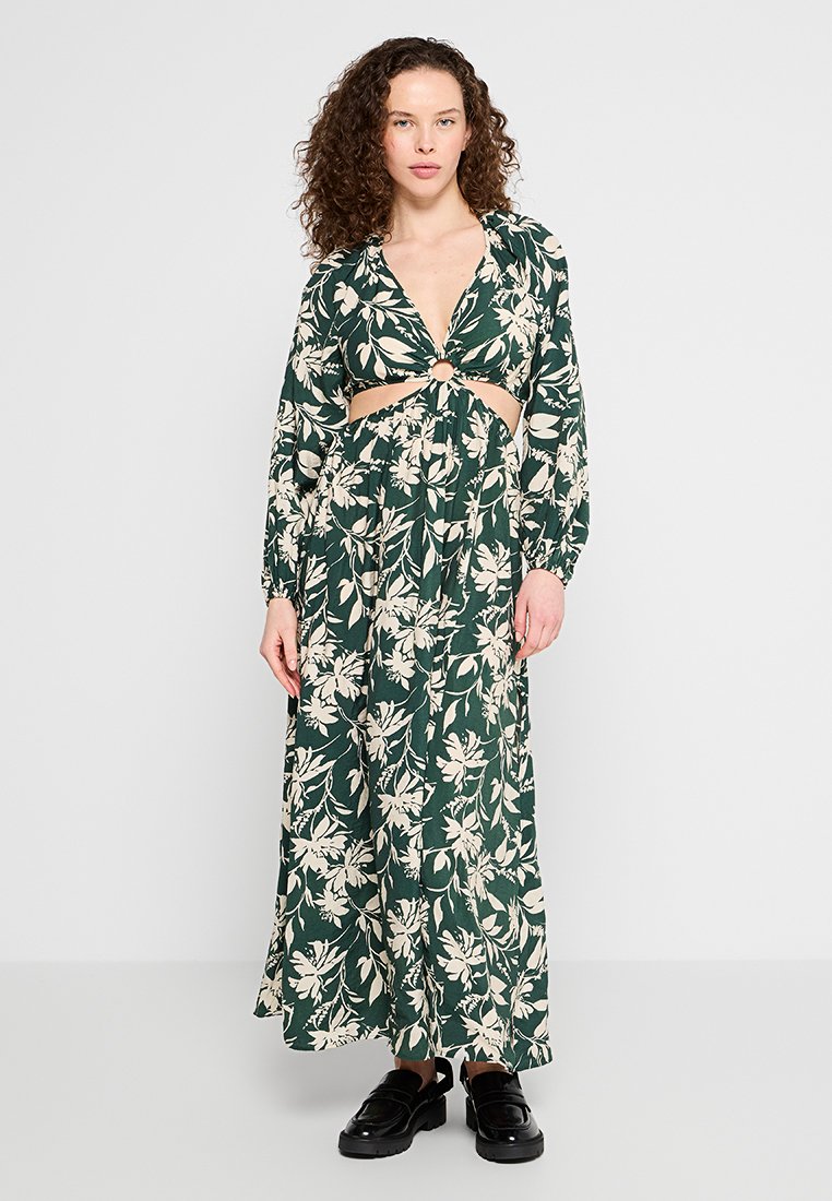 Robe maxi florale en vert foncé avec des fleurs crémeuses ; présente un design à découpe avec un accent en anneau et des manches longues ; tissu léger.