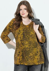 Mustakeltainen kuvioitu paita, jossa on kolme neljäsosaa hihat ja pyöreä kaula-aukko, eläinkuosilla ja väljä istuvuus.