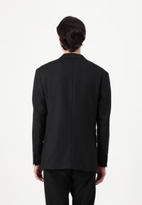 Black tailored suit jacket, structured design, notched lapel, single vent at the back, featuring buttons on cuffs, smooth fabric texture.