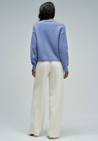 Jasnoniebieski sweter o kroju cropped z prążkowanymi mankietami, zestawiony z kremowymi spodniami z szerokimi nogawkami, wykonanymi z gładkiego, lekko płynącego materiału.