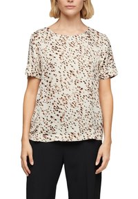 Blouse à manches courtes de couleur crème clair avec un motif à pois dans des teintes de marron. Tissu doux avec une coupe décontractée et un col rond.