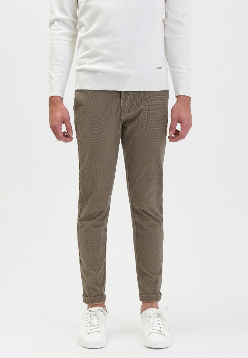 Bruine geruite broek met een slim fit, gemaakt van een gestructureerde stof. Gecombineerd met witte sneakers en een eenvoudige witte trui.