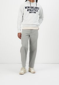 Ljusgrå sweatshirt med texten "NEW BALANCE ATHLETICS" i marinblått, i kombination med ljusgrå jeans och beige sneakers. Avslappnad sportig stil.