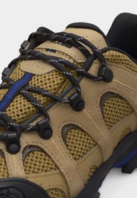 Καφέ και κίτρινο δίχτυ πεζοπορίας με κορδόνια σε μαύρο και μπλε μοτίβο περασμένα από μαύρες πλαστικές τρύπες και καφέ σουέτ επικαλύψεις.