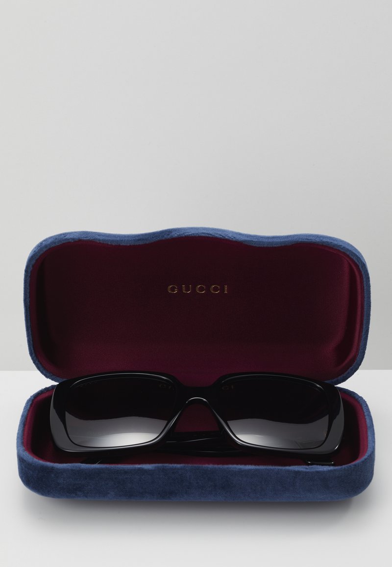 Gucci sunglasses in a dark blue velvet case with a burgundy interior, featuring bold black frames and gradient lenses.