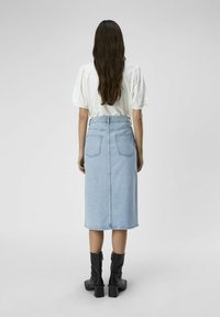 Falda de mezclilla azul clara con corte recto, dos bolsillos traseros y una cinturilla, combinada con una blusa blanca de mangas abullonadas y botas negras hasta el tobillo.