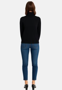 Schwarzer Rollkragenpullover mit langen Ärmeln, kombiniert mit blauen Skinny-Jeans. Das Outfit zeichnet sich durch ein figurnahes Design und eine glatte Textur aus. Schwarze High Heels runden den Look ab.