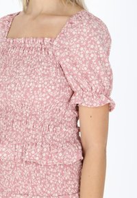 Blomstermønstrede toppe med puffærmer, kvadratisk udskæring og smock-design. Fremstillet af letvægts lyserødt stof med hvide blomsterdetaljer.