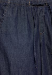 Ciemnoniebieskie dżinsy z przednimi kieszeniami, widocznym pomarańczowym przeszyciem oraz tkaninowym sznurkiem zawiązanym w talii.