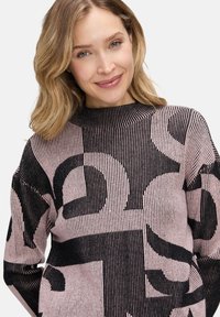 Strickpullover mit hohem Hals, geripptem Muster und einem kontrastierenden schwarzen abstrakten Muster auf einem hellrosa Hintergrund.