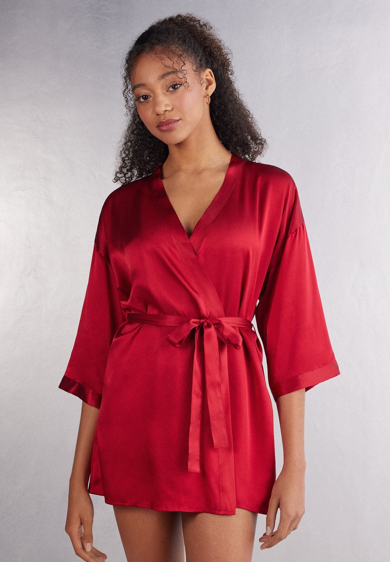 Röd sidenkimono med halvärmar, knytband i midjan och en mjuk textur. Har en subtil glans och en avslappnad passform.