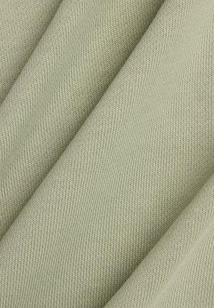 Lichtgroene textuurrijke stof met een geribbeld patroon, die een zacht, gebreid materiaal toont dat in plooien is gedrapeerd.