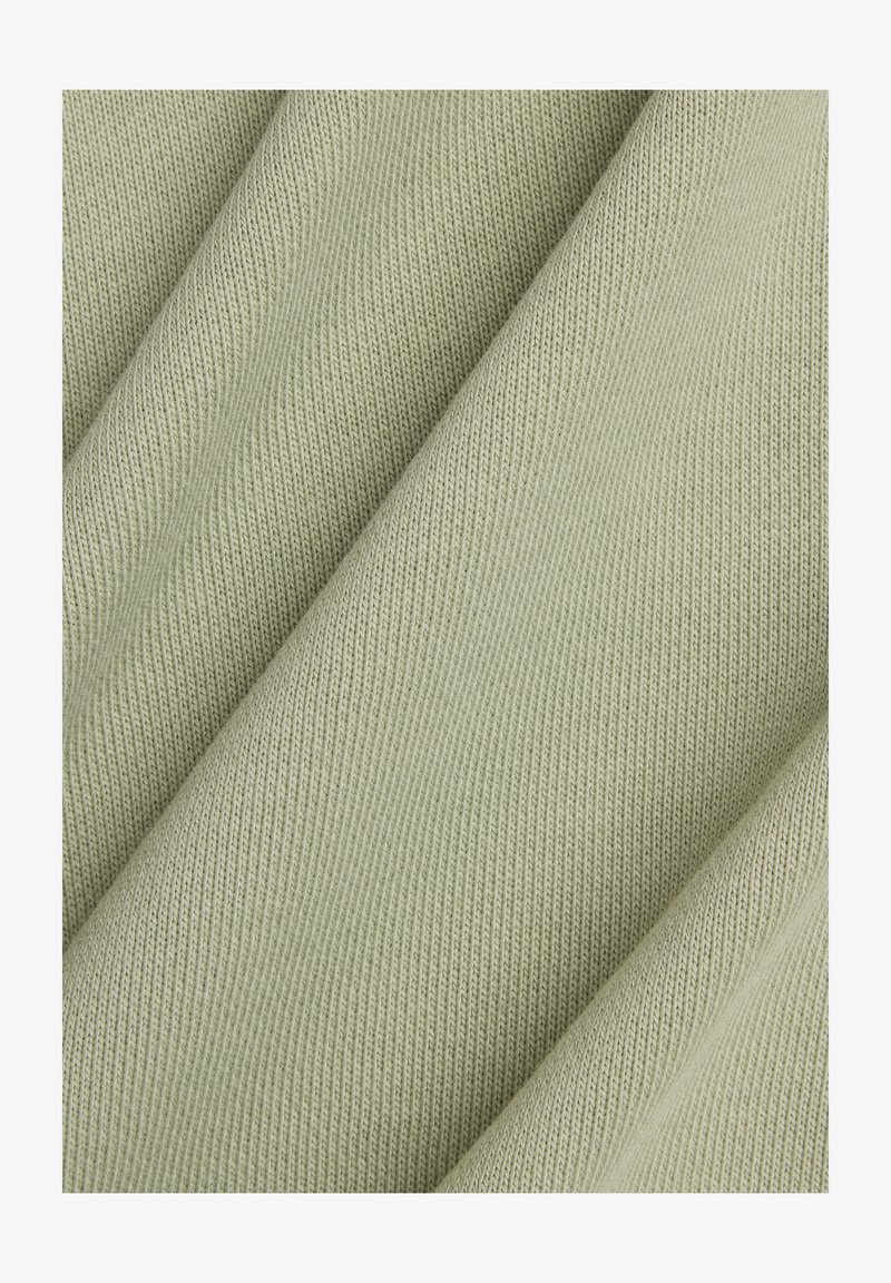 Hellgrüner, strukturierter Stoff mit einem gerippten Muster, der ein weiches, gestricktes Material zeigt, das in Falten drapiert ist.