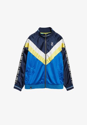 Giacca a zip blu e blu navy con strisce a zigzag gialle, bianche e blu. Presenta nastro con logo bianco e nero lungo le maniche e le tasche laterali.