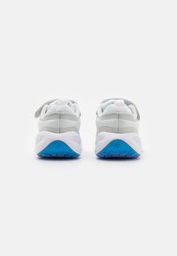Vista trasera de zapatillas deportivas blancas con detalles en gris, que cuentan con una suela texturizada en azul, un talón acolchado y correas ajustables.