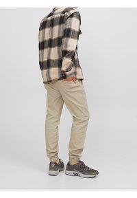 Beige-musta-laivastonsininen ruutukuvioinen flanellipaita, jossa on pitkät hihat. Yhdistetty vaaleanbeigeihin housuihin ja tummiin lenkkareihin, joissa on harmaat yksityiskohdat.