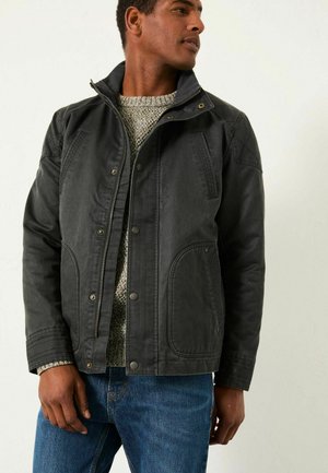 Black water-resistant jacket with zip closure, snap buttons, and side pockets. Worn over a textured grey sweater and blue jeans.