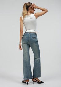 Lette denim flare jeans, falmet blå vask, med to baklommer, kombinert med en tettsittende hvit topp og svarte hæler.