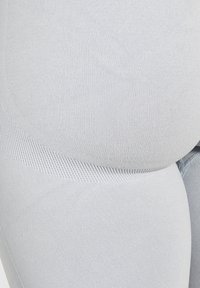 Gros plan sur un tissu gris clair texturé avec une couture courbée et des motifs de tricot variés, probablement partie d'un vêtement ou d'une garniture.