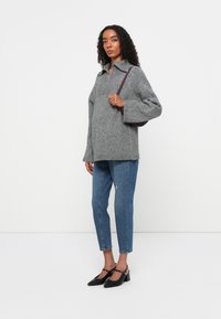Sivi vuneni oversized pulover s patent zatvaračem, uparen s svijetloslavim skinny trapericama i crnim cipelama s potpeticom. Smeđa torba na rame.
