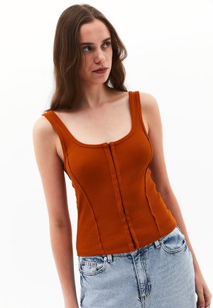 Top arancione a costine con zip frontale, design aderente e spalline larghe, abbinato a pantaloni corti di jeans blu chiaro.