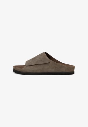 Sandale mule en daim marron à bout ouvert avec une large bride ajustable et une semelle plate noire, vue de profil sur fond blanc.