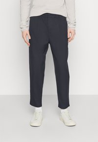 Marinblå tapered byxor med framfickor, tillverkade av lättviktsmaterial. Bärs med vita sneakers och en ljusfärgad tröja.