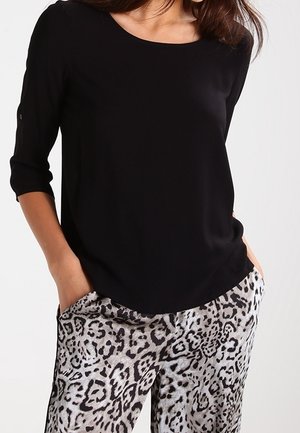 Haut noir à manches courtes avec un col rond associé à un pantalon gris à imprimé léopard présentant une texture soyeuse et une coupe ample.