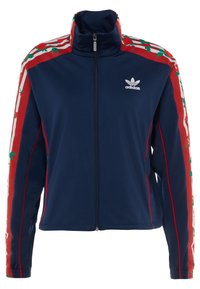 Mörkblå Adidas träningsjacka med fullständig framdragkedja, röda blommönstrade ränder på ärmarna, vit Adidas-logga på vänster bröst.