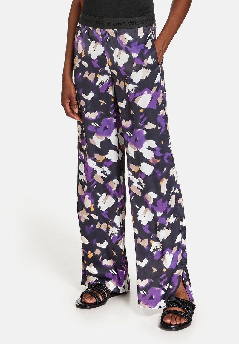 Pantalons larges en tissu léger, arborant un motif floral abstrait multicolore en violet, blanc et noir, avec une taille noire.