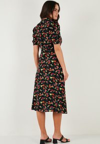 Abito nero a fiori con maniche corte a sbuffo, lungo fino al ginocchio, caratterizzato da fiori colorati in rosso, giallo e verde. Tessuto morbido con un design fluido.