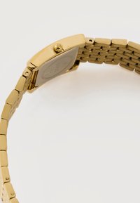 Ρολόι χειρός από μέταλλο με χρυσή απόχρωση και μπρασελέ με συνδέσμους, δείχνοντας την πίσω θήκη και το κορώνα, σε λευκό φόντο.