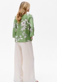 Zielona kwiatowa bluzka wykonana z lekkiego materiału, zdobiona dużymi białymi kwiatami i liśćmi. Połączona z beżowymi spodniami o szerokich nogawkach.