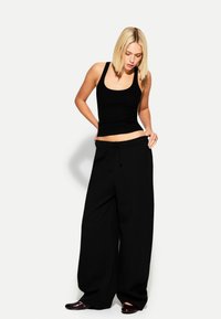Un top negru cu dungi, fără mâneci, combinat cu pantaloni largi negri. Pantalonii au un brâu elastic cu șnur. Pantofi roșii fără toc.