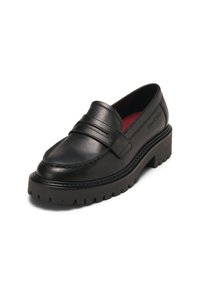 Mocassin en cuir noir avec semelle crantée épaisse, bride décorative sur le cou-de-pied et doublure intérieure rouge, présenté en angle pour montrer les détails latéraux et supérieurs.