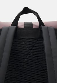 Black mesh back of a backpack with adjustable straps and a top handle. Features a smooth, soft pink upper material.