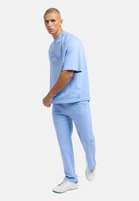 Light blue cotton short-sleeve sweatshirt and matching pants with embroidered logo, complemented by white sneakers and subtle accents.
