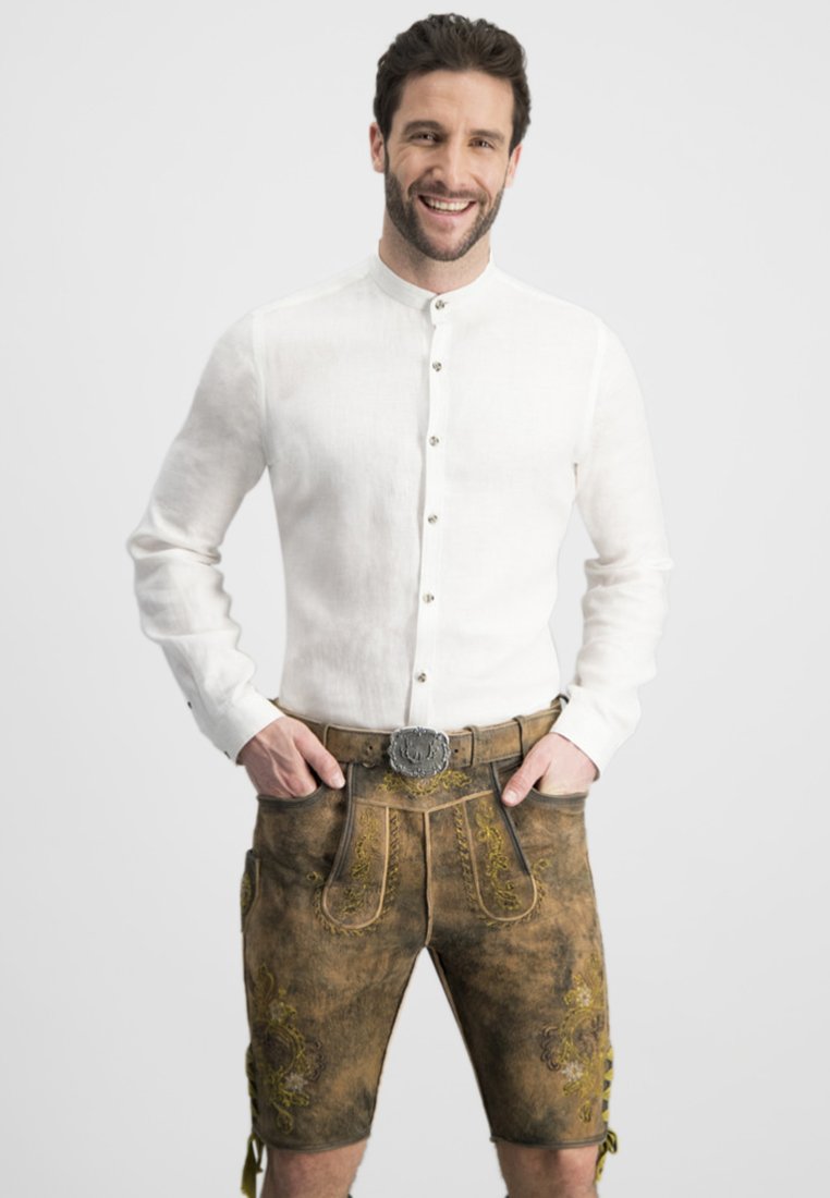 Traditionelles Outfit mit einem weißen Leinenhemd mit Knöpfen und braunen Lederhosen, verziert mit gelben Blumenstickereien und dekorativen Taschen.
