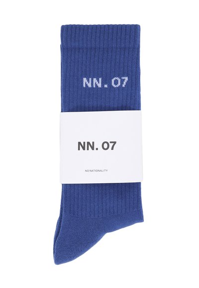 Blå ribbede bomuldsokker med en hvid tekstetiket, der viser "NN. 07" og "NO NATIONALITY" omkring den foldede kant.