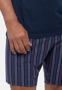 Gestreepte zwembaden in marineblauw, rood en wit. Zacht stof met een gladde textuur, voorzien van verticale strepen en een elastische tailleband.