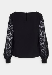 Schwarze Bluse mit solidem Körper und durchsichtigen langen Ärmeln aus schwarzer Spitze. Mit rundem Ausschnitt und einer Schlüsselbeingröße hinten.