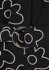 Tissu noir avec des fleurs dessinées en blanc et une boucle double anneau argentée fermant une ceinture assortie à motif floral.