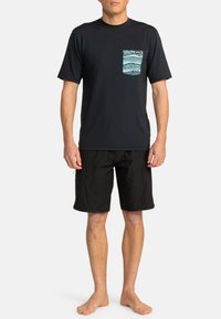 Svart t-shirt med kort ärm och en mönstrad blå ficka samt lätta svarta shorts. Båda plaggen har en avslappnad, ledig design.