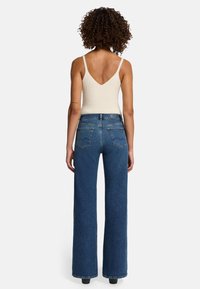 Top in cotone ribbed beige chiaro con spalline sottili, abbinato a jeans a vita alta blu scuro con gamba larga, dotati di tasche posteriori e dettagli di cucitura.