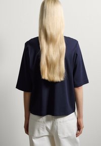 Navyblauwe kortärmige top met een ontspannen pasvorm, gemaakt van zachte katoen, gecombineerd met witte hoge taille broeken. Glad textuur, minimalistisch ontwerp.