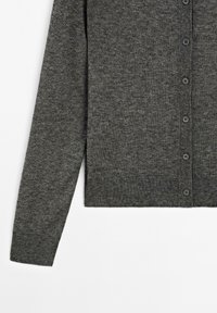 Cardigan gris avec une texture douce, des manches longues et un devant à boutons. Présente des boutons espacés uniformément le long du centre et un ourlet droit.