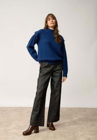 Niebieski sweter wykonany na drutach z wysokim kołnierzem, w połączeniu z ciemnoniebieskimi spodniami o szerokich nogawkach z kontrastowym przeszyciem oraz brązowymi botkami na słupku.