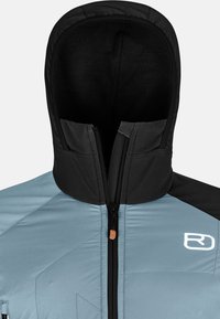 Light blue puffer jacket with a black hood and collar, featuring a front zipper and reflective logo. Textured, insulated fabric with geometric patterns.
