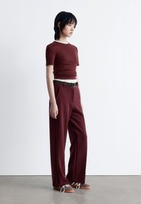 Burgundy fitted t-shirt with short sleeves, paired with high-waisted, wide-leg trousers in the same color and a black belt. Brown sneakers.