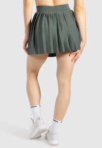 Falda plisada verde de cintura alta, hecha de una tela suave. Combinada con zapatillas blancas y calcetines con estampado.